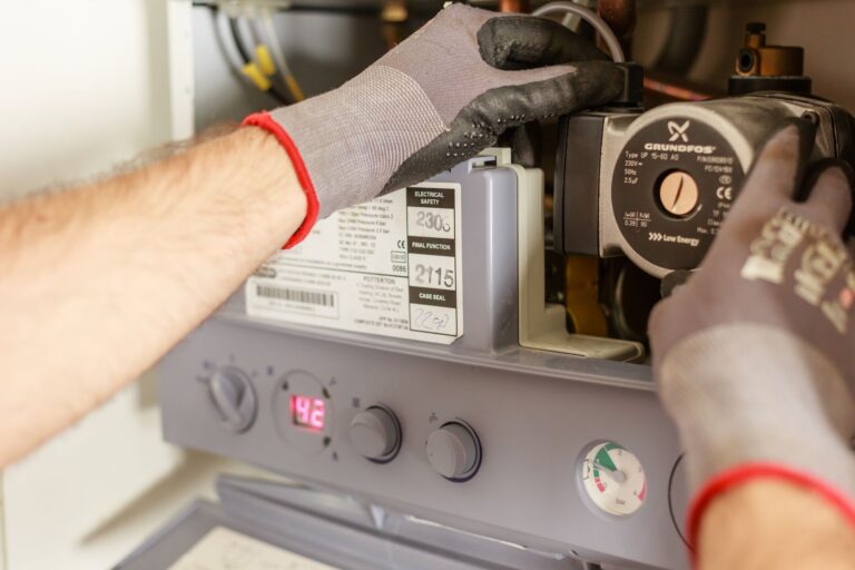 VVS-tekniker med arbejdshandsker efterser cirkulationspumpe og tryk i et gasfyr for at finde energibesparelser