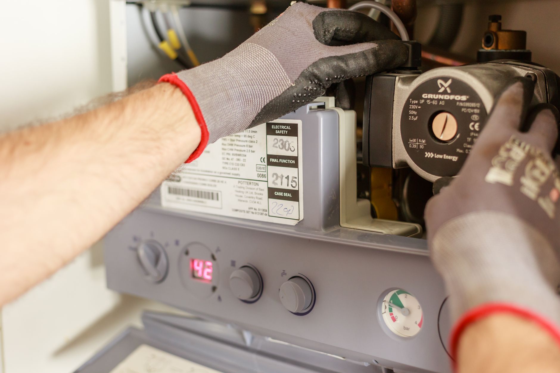 VVS-tekniker med arbejdshandsker efterser cirkulationspumpe og tryk i et gasfyr for at finde energibesparelser